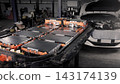 EV car service. Electric vehicle battery pack being serviced or inspected in automotive workshop. Large battery modules and high voltage components. Modern EV power systems. Lithium ion NMC NCA or LFP 143174139
