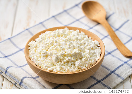 Fresh cottage cheese in a wooden bowl on a white table, selective focus. Fresh cottage cheese in a wooden bowl on a white table, selective focus. 143174752