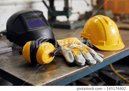 Essential industrial safety equipment including a welding helmet and hard hat on a metal workbench Essential industrial safety equipment including a welding helmet and hard hat on a metal workbench 143174802