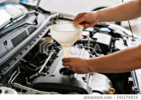 Mechanic pouring fresh motor oil into a car engine using a plastic funnel for maintenance Mechanic pouring fresh motor oil into a car engine using a plastic funnel for maintenance 143174819