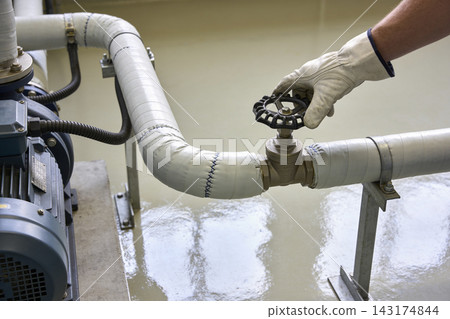 Industrial worker adjusting a manual gate valve on a pipe system in a manufacturing facility Industrial worker adjusting a manual gate valve on a pipe system in a manufacturing facility 143174844