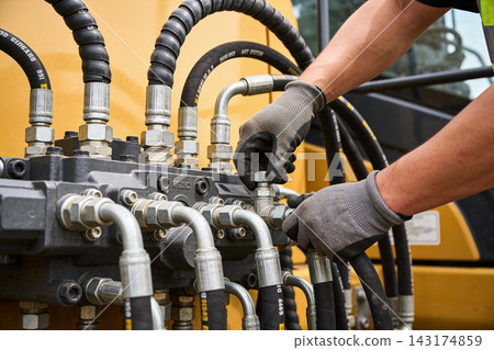 Mechanic performing maintenance on heavy construction machinery hydraulic system components 143174859