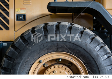 Close up of a heavy duty construction vehicle tire with a rugged tread pattern and yellow rim Close up of a heavy duty construction vehicle tire with a rugged tread pattern and yellow rim 143174924
