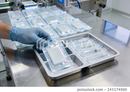 Technician in blue gloves inspecting medical supplies on a stainless steel production line table Technician in blue gloves inspecting medical supplies on a stainless steel production line table 143174980