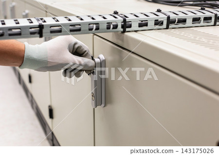 Technician wearing protective gloves opening a metal electrical cabinet in a facility Technician wearing protective gloves opening a metal electrical cabinet in a facility 143175026