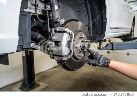 Mechanic inspecting the disc brake assembly of a lifted vehicle in a professional repair garage Mechanic inspecting the disc brake assembly of a lifted vehicle in a professional repair garage 143175066
