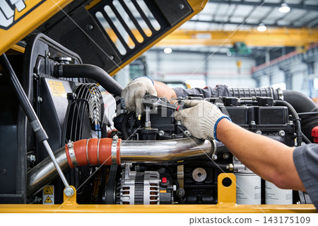 Mechanic using a ratchet tool to repair the engine of a heavy yellow construction machine inside Mechanic using a ratchet tool to repair the engine of a heavy yellow construction machine inside 143175109