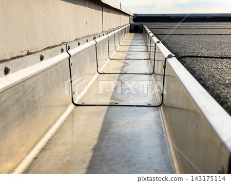 Close up of a metal roof gutter system installed on a flat building roof for water drainage Close up of a metal roof gutter system installed on a flat building roof for water drainage 143175114