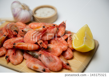 A close-up side view of frozen shrimps on a wooden board, two lemon slices diagonally, a salt shaker and a head of garlic next to it. Concept: an expanded set of seafood seasonings. High quality photo A close-up side view of frozen shrimps on a wooden board, two lemon slices diagonally, a salt shaker and a head of garlic next to it. Concept: an expanded set of seafood seasonings. High quality photo 143175321