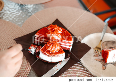 Red Velvet cake slices on a table. Delicious dessert with cream cheese frosting, hand with fork, cafe setting, sweet treat food. 143175806