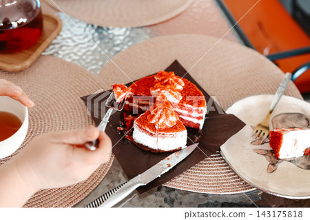 Red Velvet cake slices on a table. Delicious dessert with cream cheese frosting, hand with fork, cafe setting, sweet treat food. Red Velvet cake slices on a table. Delicious dessert with cream cheese frosting, hand with fork, cafe setting, sweet treat food. 143175818