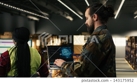 Military officer using AI-powered tools in warehouse at military base, monitoring artificial intelligence software on laptop. Machine learning and neural networks supporting tactical operations. Military officer using AI-powered tools in warehouse at military base, monitoring artificial intelligence software on laptop. Machine learning and neural networks supporting tactical operations. 143175952