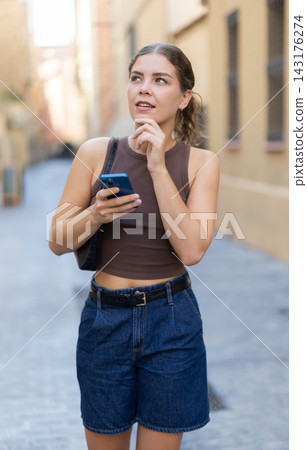 Girl walks around city district with mobile phone Girl walks around city district with mobile phone 143176274