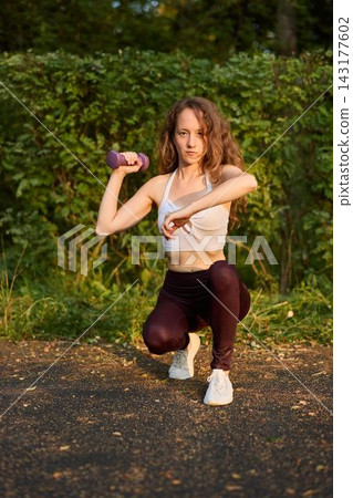 Young Female Focusing On Rehabilitation Exercises Using Dumbbells In Peaceful Park Surroundings Young Female Focusing On Rehabilitation Exercises Using Dumbbells In Peaceful Park Surroundings 143177602