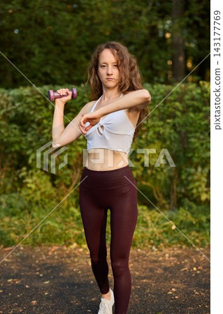 Young lady performs dynamic upper body stretch in park setting 143177769