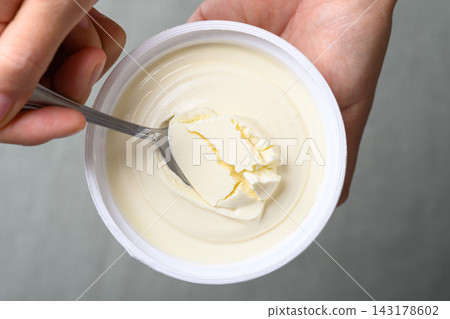 Hand holding a spoon and scooping fresh cream cheese in a cup, top view 143178602