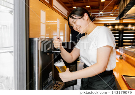 A young female part-timer pouring beer from a beer dispenser. 143179079