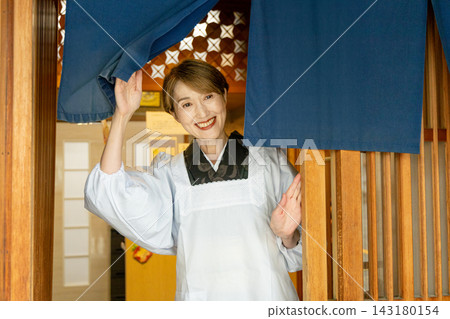 一位穿著和服的老婦人拉開暖簾,微笑著迎接顧客。 一位穿著和服的老婦人拉開暖簾,微笑著迎接顧客。 143180154