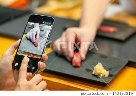 一位女士用智慧型手機拍照,以紀念她造訪高級壽司店的經歷。 一位女士用智慧型手機拍照,以紀念她造訪高級壽司店的經歷。 143183819