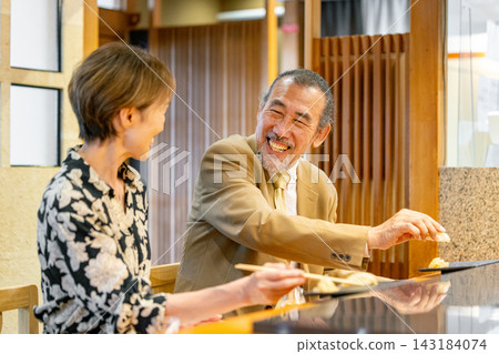 A senior couple and the chef at a sushi restaurant A senior couple and the chef at a sushi restaurant 143184074
