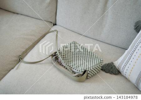 A green textured bag placed on a light gray couch with a pillow nearby 143184978