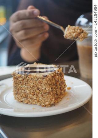 A woman is eating a piece of cake with a spoon in a cafe A woman is eating a piece of cake with a spoon in a cafe 143184984