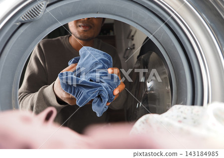 Man removing laundry from washer in a home setting during daytime Man removing laundry from washer in a home setting during daytime 143184985