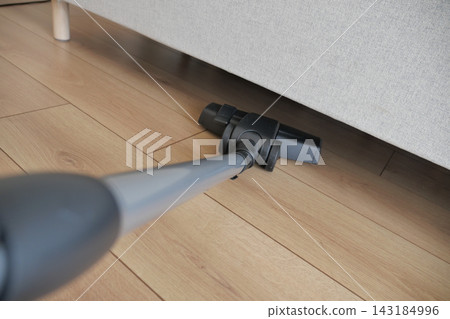 Person vacuuming under couch in living room during daytime Person vacuuming under couch in living room during daytime 143184996