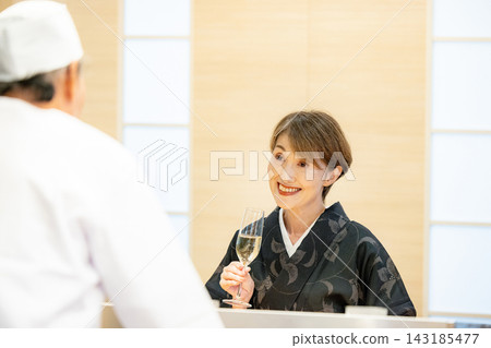 A senior female customer chatting with the sushi chef at the counter. A senior female customer chatting with the sushi chef at the counter. 143185477