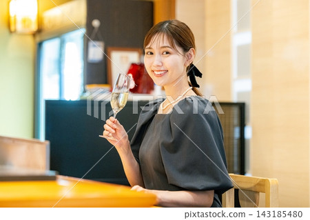 一位年輕女子坐在吧台邊,手裡拿著一杯香檳。 一位年輕女子坐在吧台邊,手裡拿著一杯香檳。 143185480