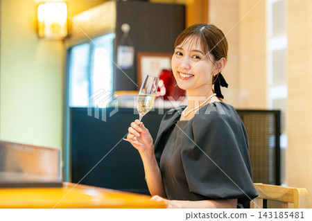 一位年輕女子坐在吧台邊,手裡拿著一杯香檳。 一位年輕女子坐在吧台邊,手裡拿著一杯香檳。 143185481