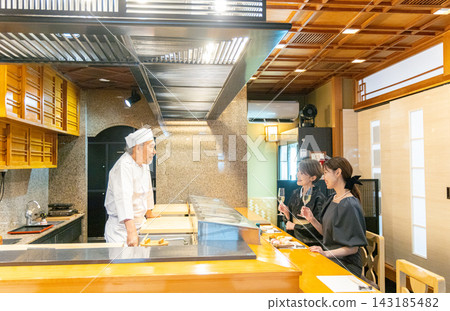 一對舉止優雅的父母帶著孩子在壽司店與壽司師傅交談。 143185482