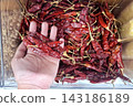 Handful of dried organic red chili peppers held over container of bulk spices for culinary cooking preparation and traditional spicy flavor ingredient. 143186189
