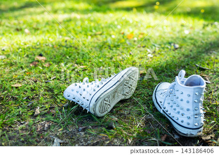 White studded high-top sneakers placed on green grassy park lawn with sunlit bokeh background, scattered fallen leaves, shallow depth of field outdoors fashion footwear lifestyle White studded high-top sneakers placed on green grassy park lawn with sunlit bokeh background, scattered fallen leaves, shallow depth of field outdoors fashion footwear lifestyle 143186406