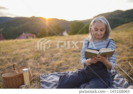 Older woman enjoying peaceful solo picnic and reading in countryside. Older woman enjoying peaceful solo picnic and reading in countryside. 143188065