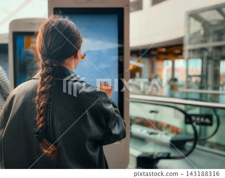 Rear view of teenage girl with braided hair standing in front of large self service interactive menu. Concept of modern automated dining, consumer choices, and teen lifestyle in urban environment. Rear view of teenage girl with braided hair standing in front of large self service interactive menu. Concept of modern automated dining, consumer choices, and teen lifestyle in urban environment. 143188316