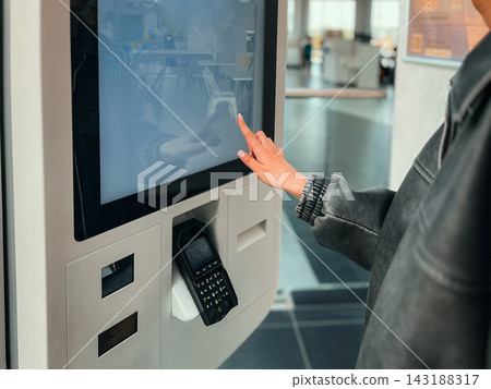 Teenage girl using touch screen interactive display to order food at self service kiosk. Concept of automated ordering system, youth using technology, and fast food digital experience. Teenage girl using touch screen interactive display to order food at self service kiosk. Concept of automated ordering system, youth using technology, and fast food digital experience. 143188317
