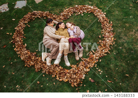 Mother, grandmother and daughter, laying on grass in the middle of heart from leaves. Mother, grandmother and daughter, laying on grass in the middle of heart from leaves. 143188333