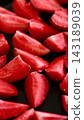 A close-up shot of strawberry pieces on a black baking sheet. 143189039