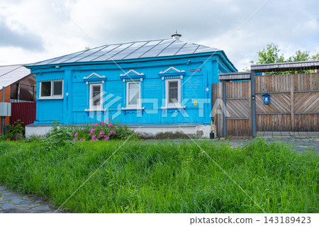 A tranquil blue wooden house in a suburban residential area, featuring a metal roof and wooden fence, viewed from the side. The serene natural setting and clean surroundings make it. A tranquil blue wooden house in a suburban residential area, featuring a metal roof and wooden fence, viewed from the side. The serene natural setting and clean surroundings make it. 143189423