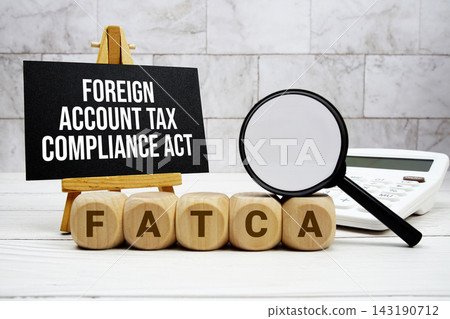 FATCA Foreign Account Tax Compliance Act text with calculator magnifying glass and on wooden background 143190712