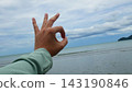 Hand Showing OK Sign Against Ocean and Sky Background 143190846