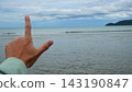 Hand Making L Shape Sign Against Ocean and Sky Background 143190847