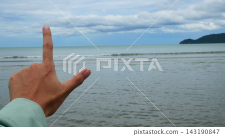 Hand Making L Shape Sign Against Ocean and Sky Background Hand Making L Shape Sign Against Ocean and Sky Background 143190847