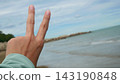 Hand Showing Victory Peace Sign Against Ocean and Sky Background 143190848