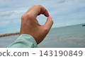 Hand Making Circle Shape Sign Against Ocean and Sky Background 143190849