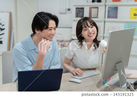 一對年輕男女一邊看著電腦螢幕一邊交談——這是創意團隊作品中的一個場景。 一對年輕男女一邊看著電腦螢幕一邊交談——這是創意團隊作品中的一個場景。 143191325
