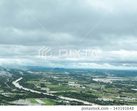 Rain clouds blanket swollen river winding through lush agricultural fields, dense mist rolls across the flooded rural landscape in gloomy monsoon day. Rain clouds blanket swollen river winding through lush agricultural fields, dense mist rolls across the flooded rural landscape in gloomy monsoon day. 143191648