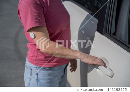 A woman with a continuous glucose monitor on her arm gets into a car. 143192255