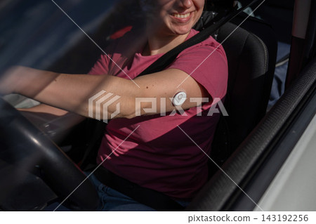 A woman wearing a continuous glucose monitor is driving a car. A woman wearing a continuous glucose monitor is driving a car. 143192256